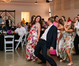 Guests dancing at a reception, with women in floral dresses and a man in a dark suit in the foreground