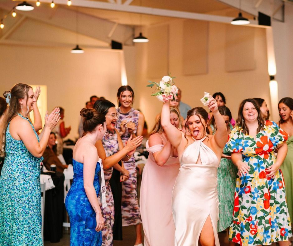 Bride tossing bouquet to a group of cheering guests in a warmly lit reception hall