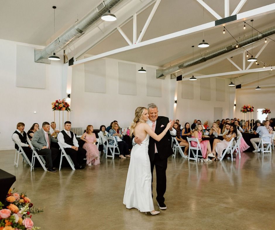 Bride and groom dancing in a bright reception hall with seated guests watching