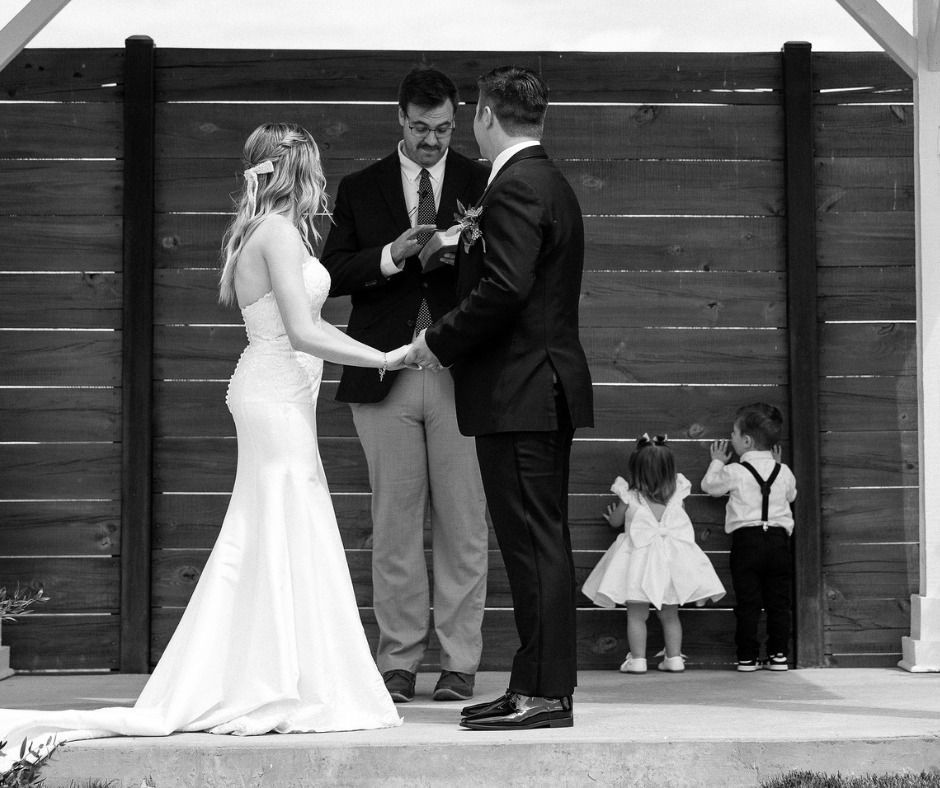 Bride and groom exchanging vows at an outdoor wedding ceremony while two children stand nearby