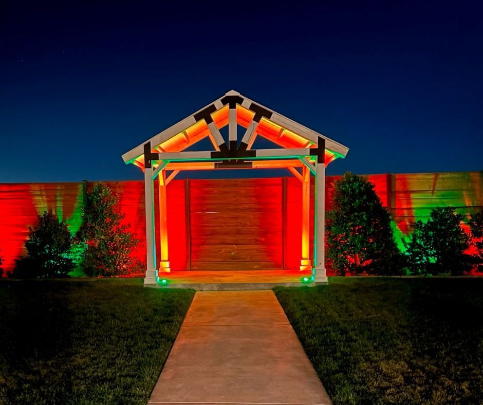 Colorfully lit house facade with red and green lights, a central wooden gate, and a walkway at night