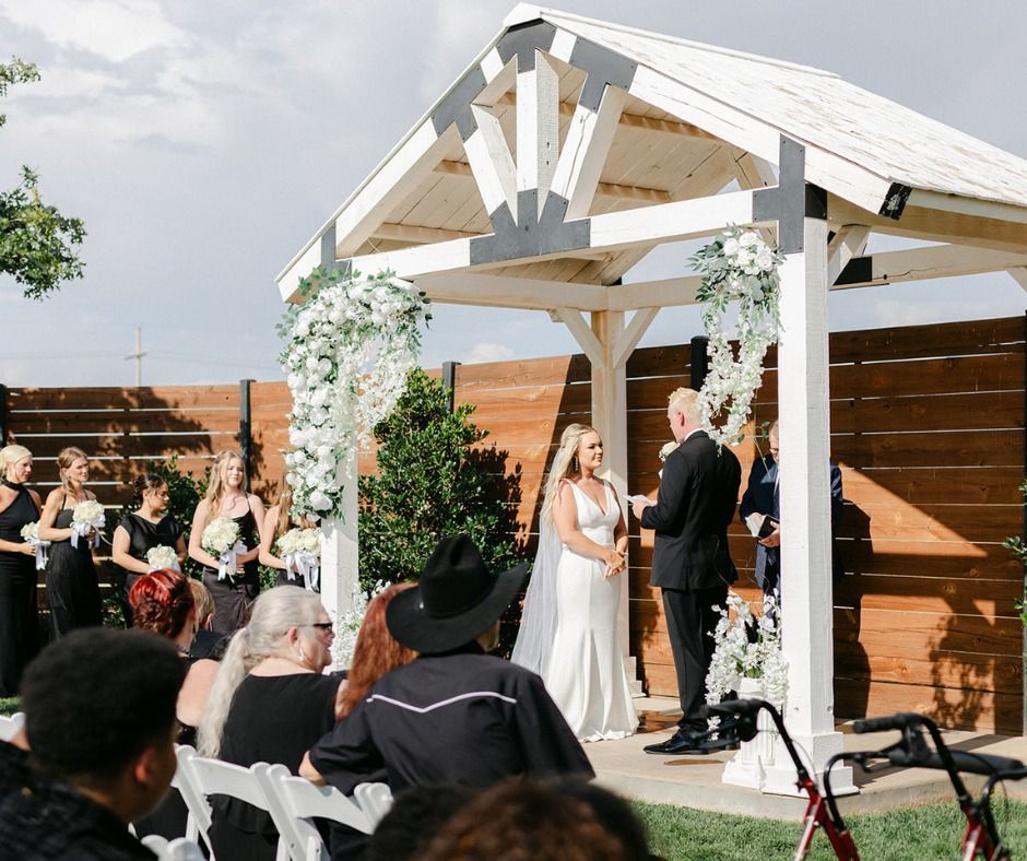 Outdoor wedding ceremony under a white pergola with bride, groom, and officiant on a wooden patio