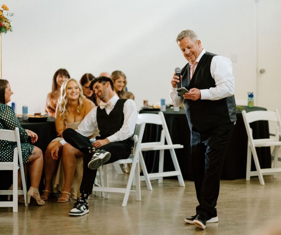 Presenter speaking to seated audience in a bright room, holding a microphone beside white folding chairs.