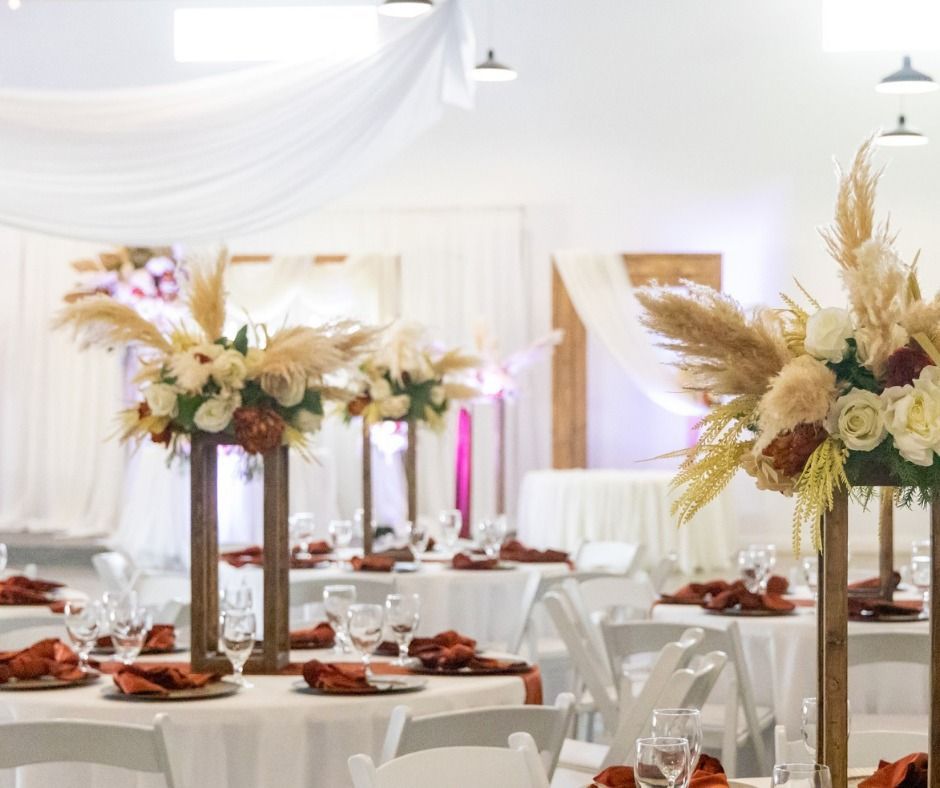 Elegant wedding reception tables with white chairs and floral centerpieces in a bright, draped venue