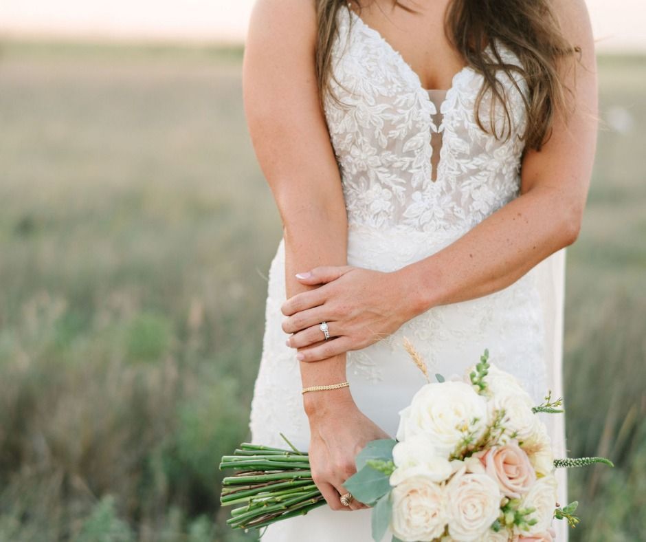 Bridal bouquet held by a woman in a white lace wedding dress in a grassy outdoor setting