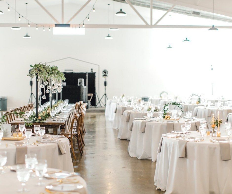 Elegant wedding reception hall with white table settings and round tables under high ceilings