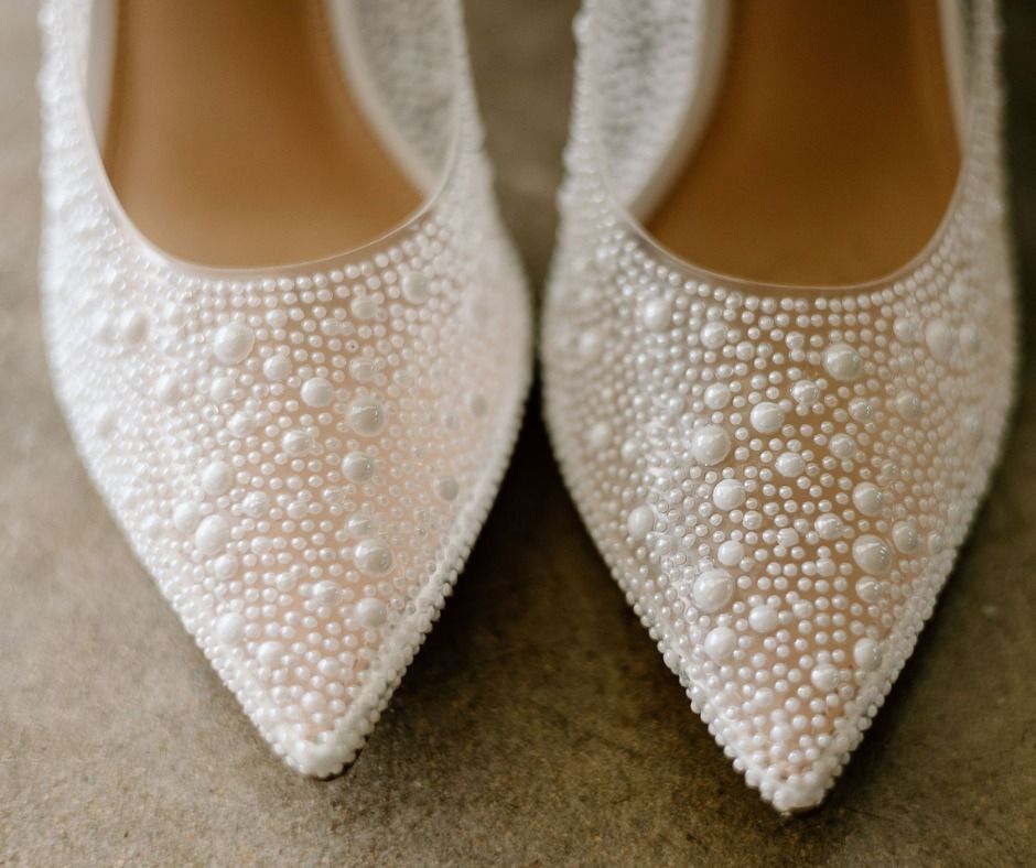 Pearl-embellished ivory pointed-toe flats on a neutral fabric background