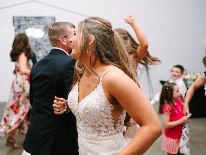 Wedding guests dancing at a reception, with a bride in a white lace dress in the foreground.