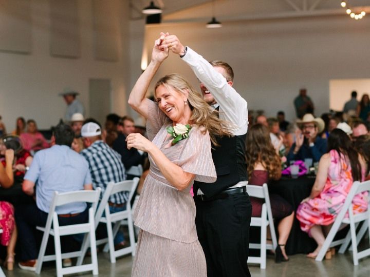 Couple dancing at a lively indoor reception with guests seated at tables nearby