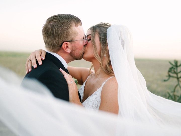 Bride and groom kissing outdoors, bride in a white veil and gown, soft beach background