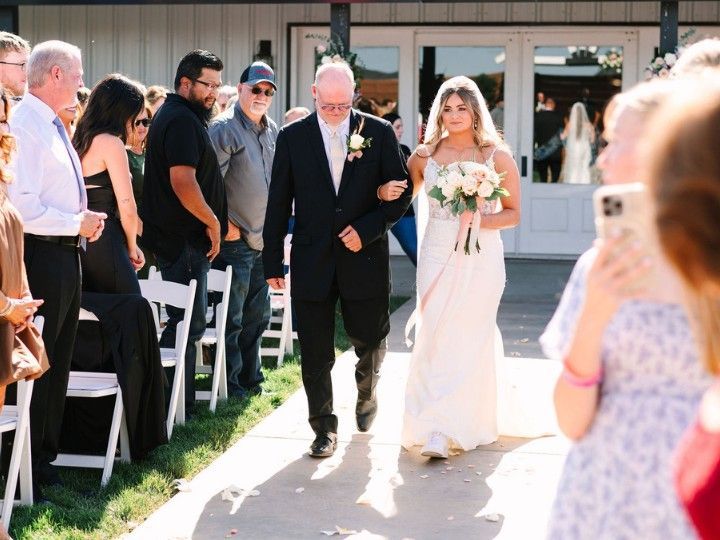 Wedding procession outdoors with a bride in white and a man in a dark suit walking down the aisle