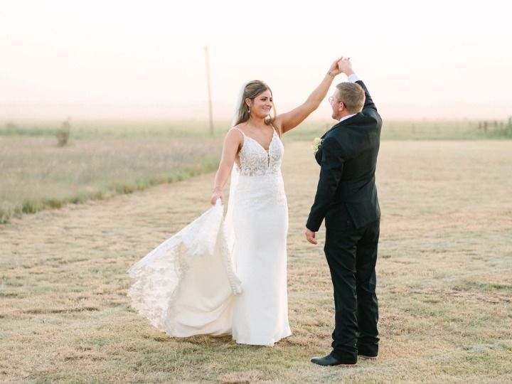 Couple in wedding attire dancing outdoors in a field at sunset