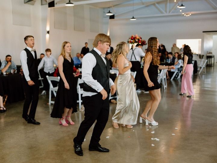 People dancing at a wedding reception in a bright indoor hall, with guests seated in the background