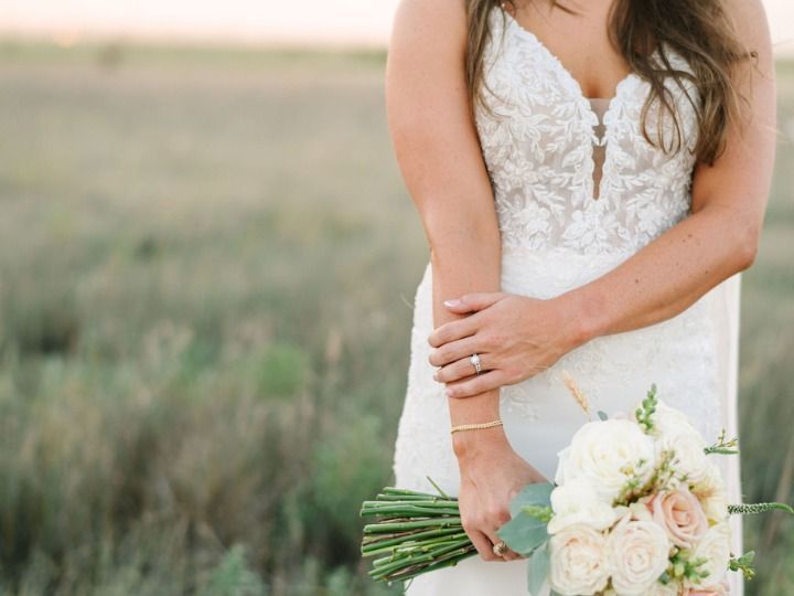Bride in a white lace dress holding a bouquet of white roses in a field