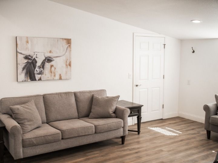 Living room with gray sofa, side table, wall art, white door, and wood-look floor