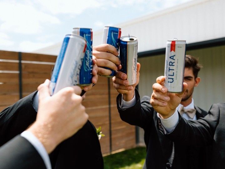 People in suits clink silver cans together in a celebratory toast outdoors.