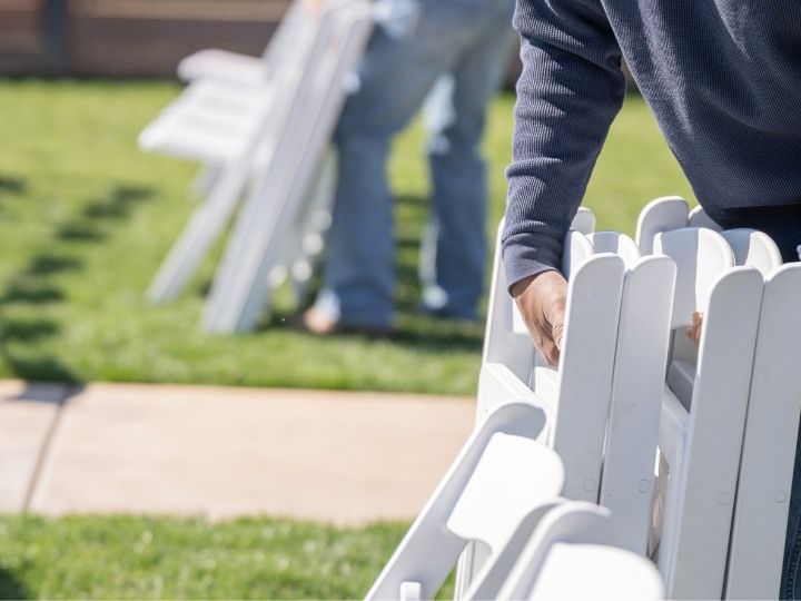 Person carrying a white picket fence panel on a grassy lawn near a sidewalk