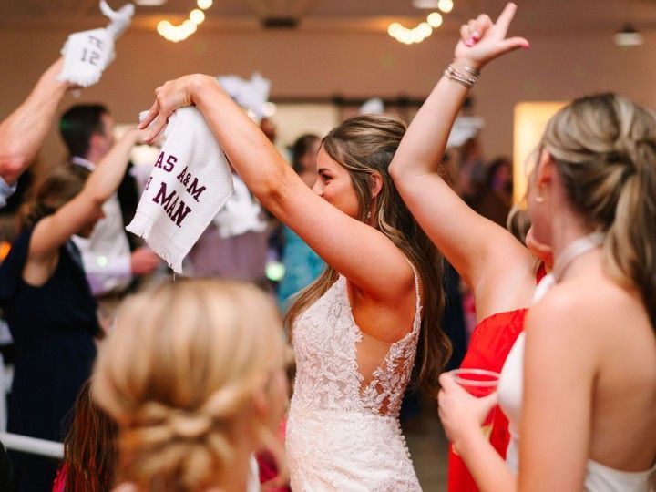 Woman in a lace dress dancing at a lively indoor celebration with raised arms and guests around her