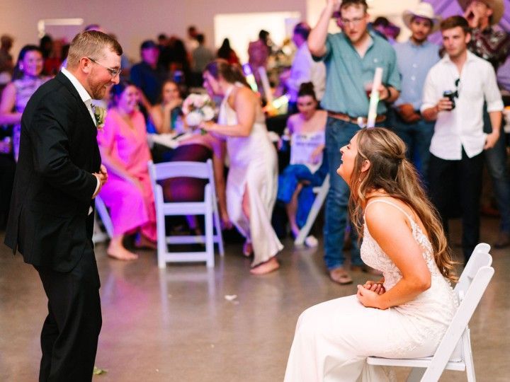 Man in a suit speaking to a seated woman in a white dress at a lively indoor event