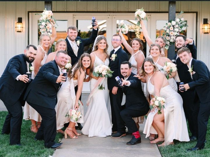 Wedding party posing outdoors in front of a wooden barn, holding bouquets and smiling.