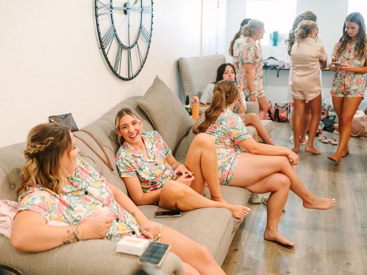 Group of women in matching floral outfits relaxing in a bright living room, chatting on couches and standing nearby