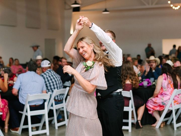 Couple dancing at a reception, smiling in a bright hall with seated guests in the background