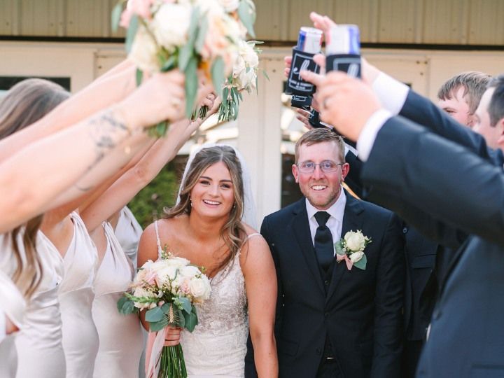 Bride and groom smiling beneath raised bouquets at an outdoor wedding ceremony