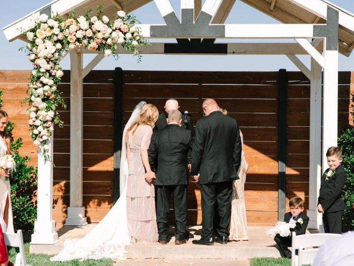Wedding ceremony under floral arch with guests and children in a wooden pavilion