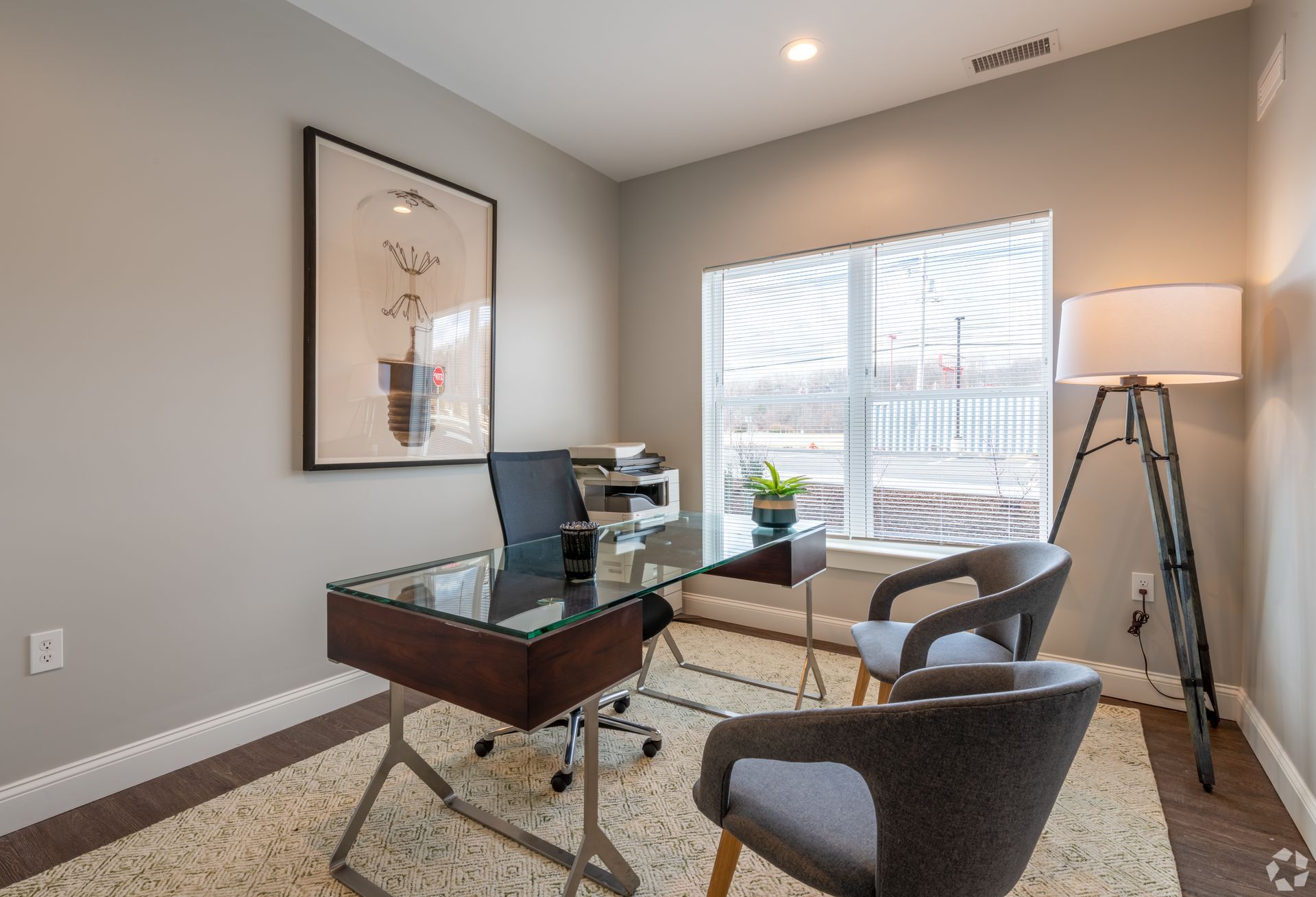 a home office with a desk , chairs and a large window .