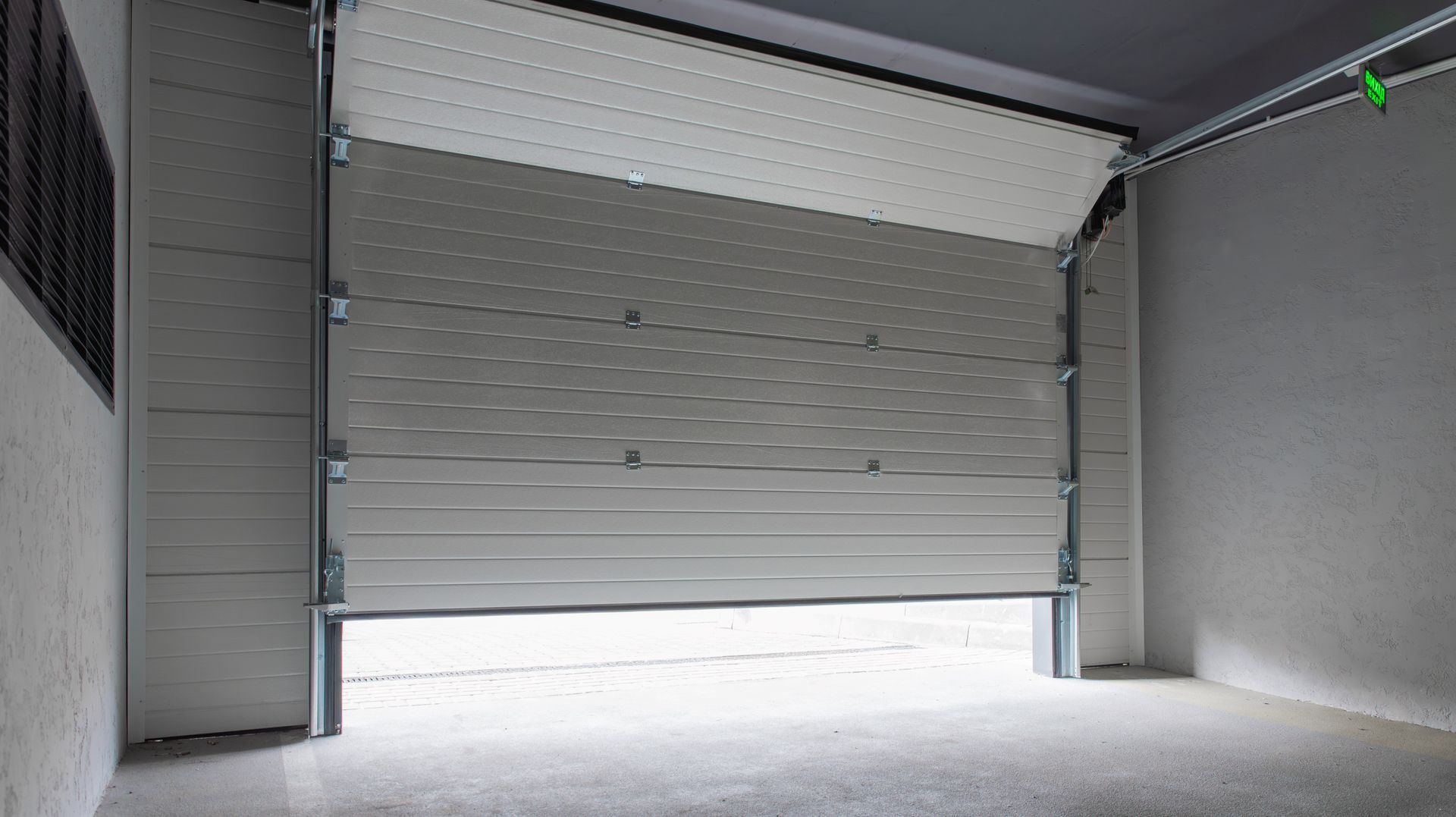 Empty industrial garage with a partially open gray roll-up door and concrete floor.