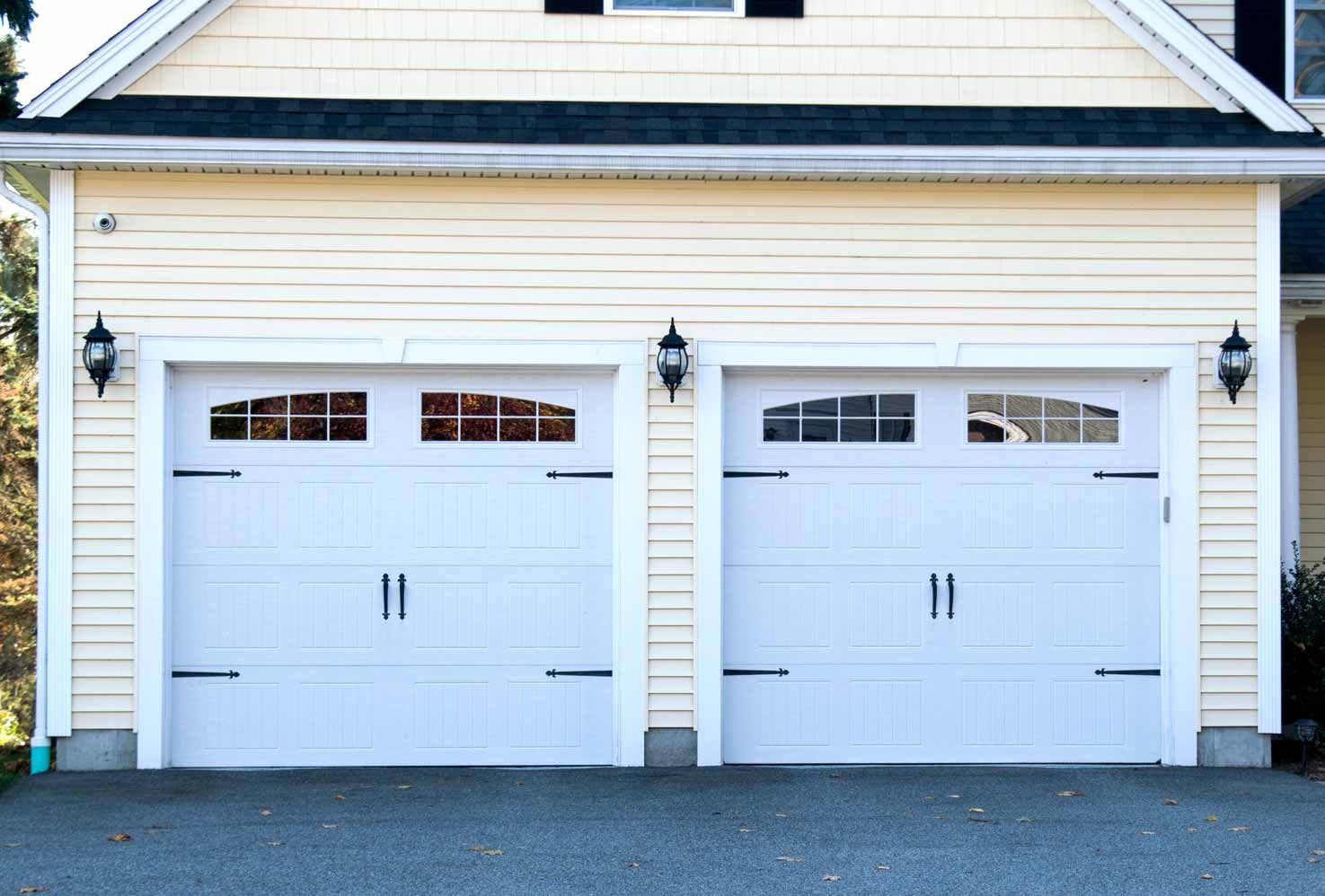 Two white garage doors on a beige house exterior with black wall lanterns.