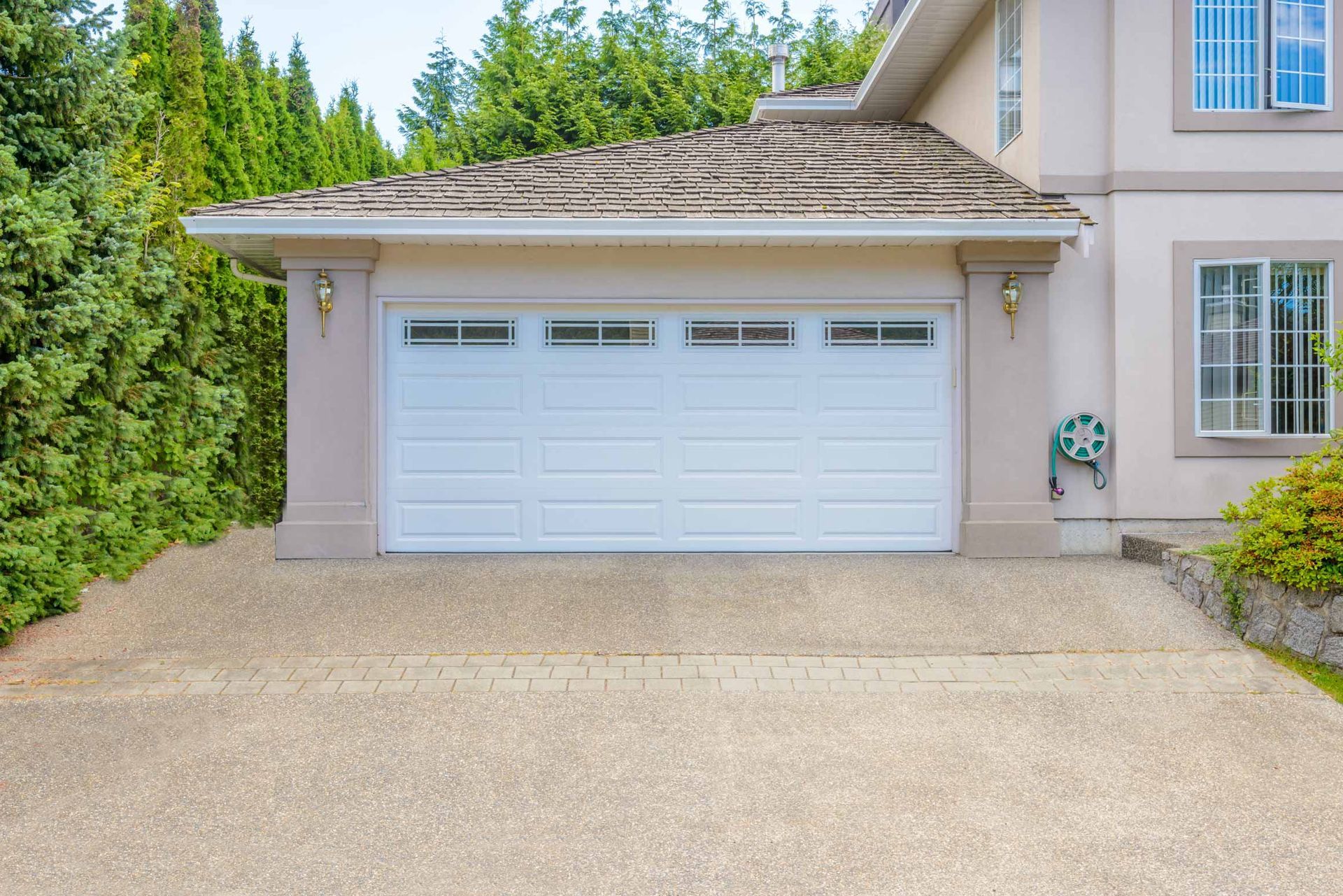 Suburban home exterior with a white garage door, gravel driveway, and trees lining the side yard