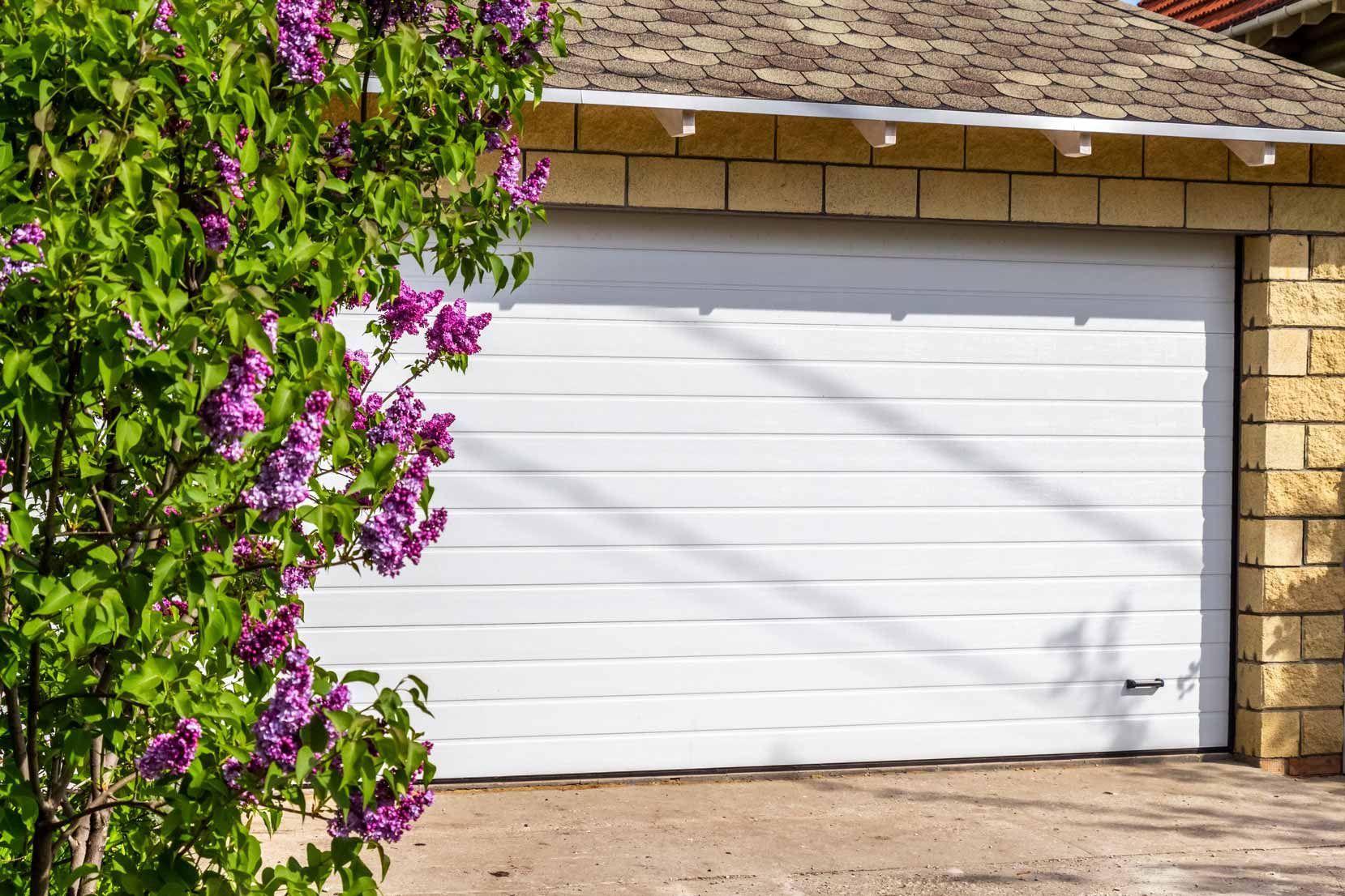 White garage door beside a flowering purple bougainvillea vine under a tiled roof