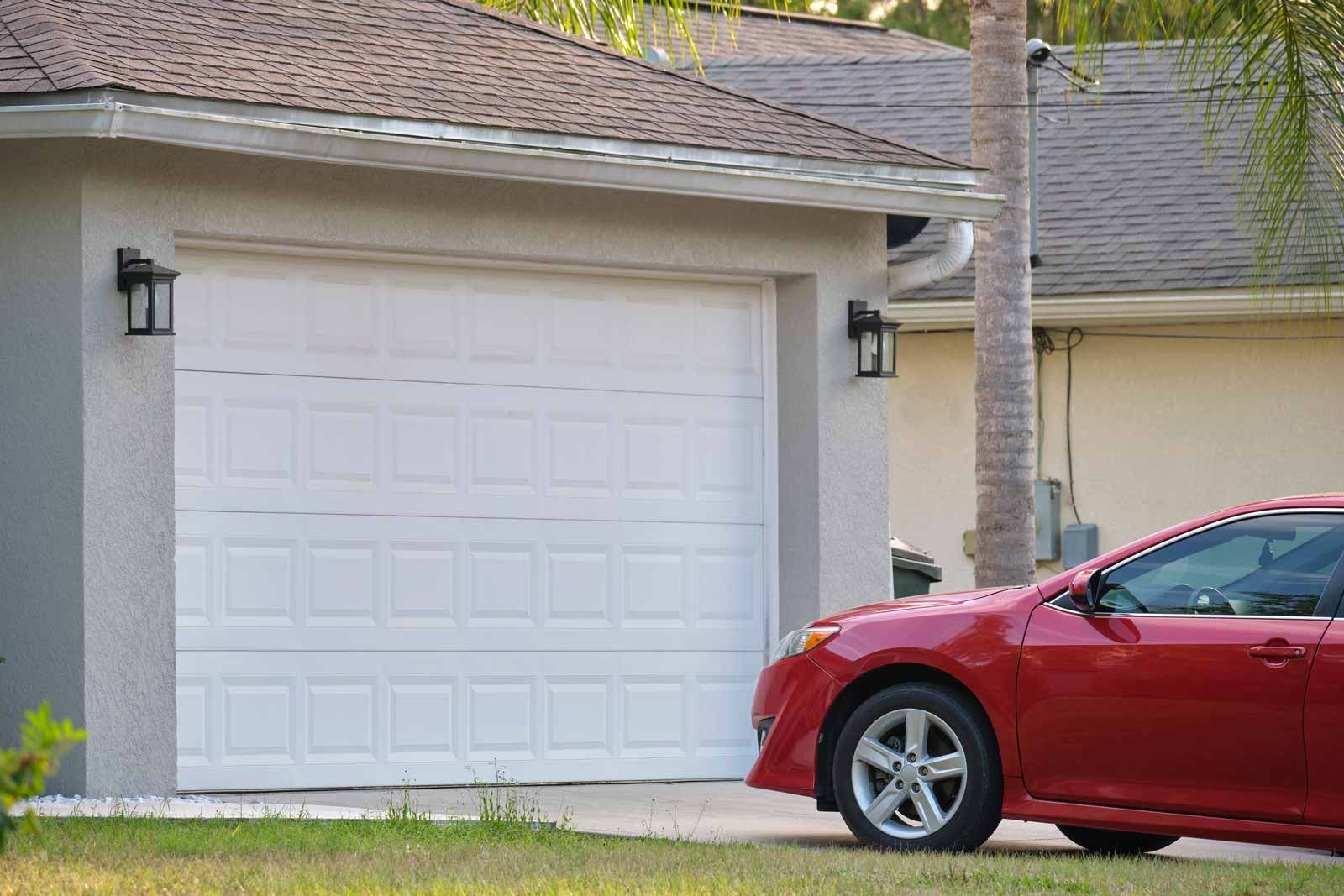 Red car parked in front of a white garage door in a suburban driveway.
