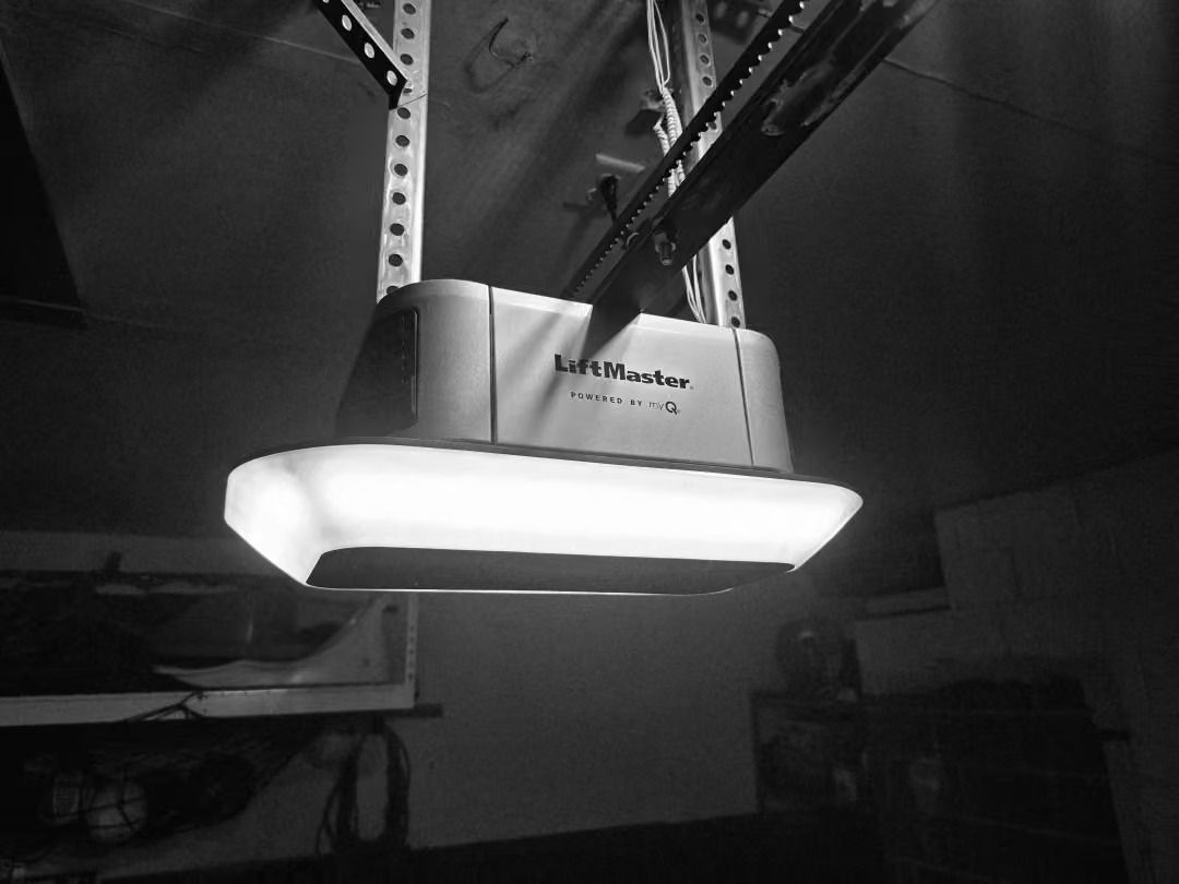 Ceiling-mounted garage door opener with bright light shining downward in a dark room