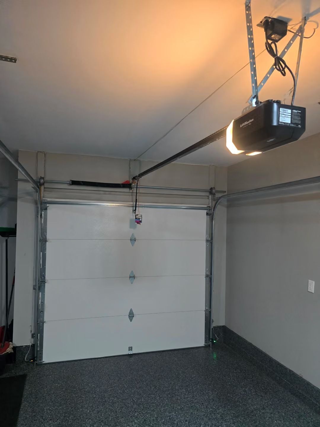 Empty residential garage with a closed white overhead door and ceiling-mounted garage door opener.