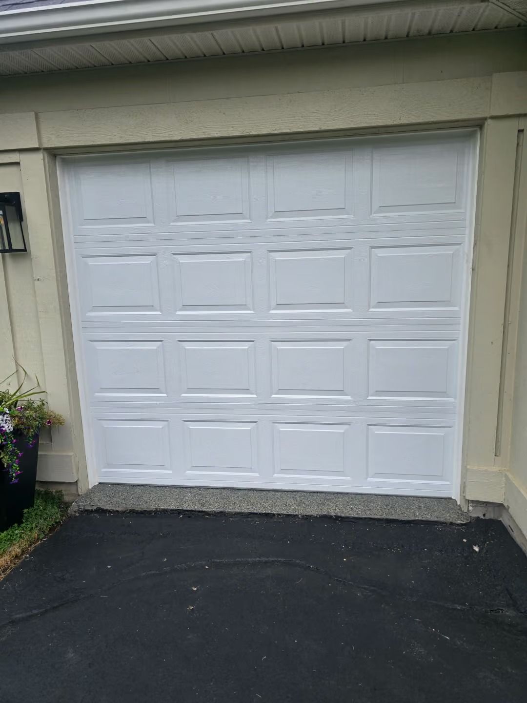 White paneled garage door on a beige house, viewed from a driveway.
