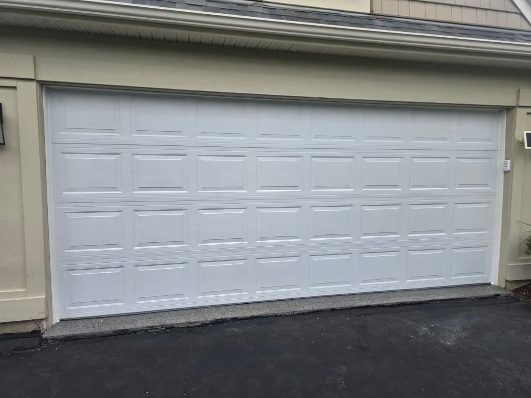 White double garage door on a beige house, viewed from the driveway.
