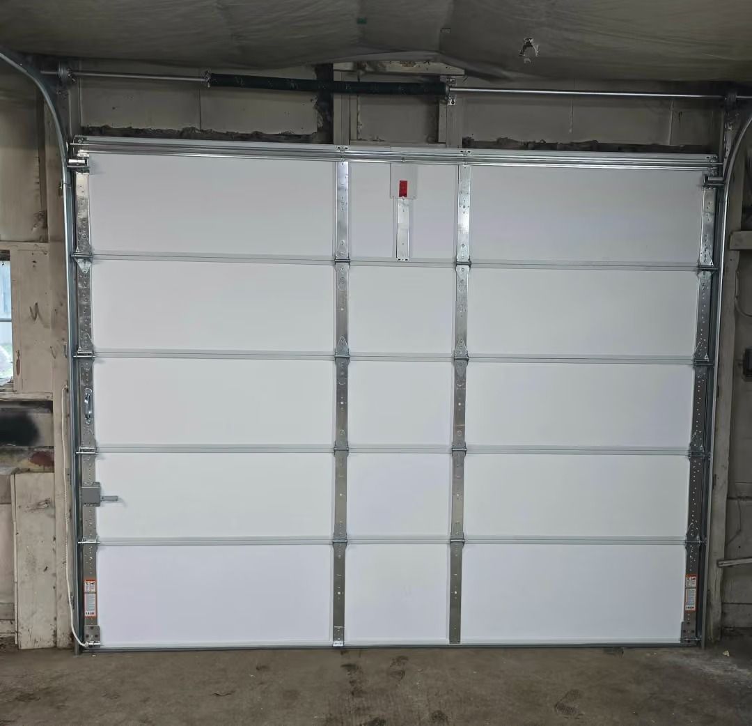 White garage door with a small red alarm in an unfinished concrete bay