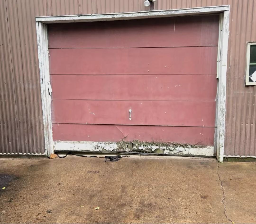 Weathered red garage door on a corrugated metal building above a wet concrete pad