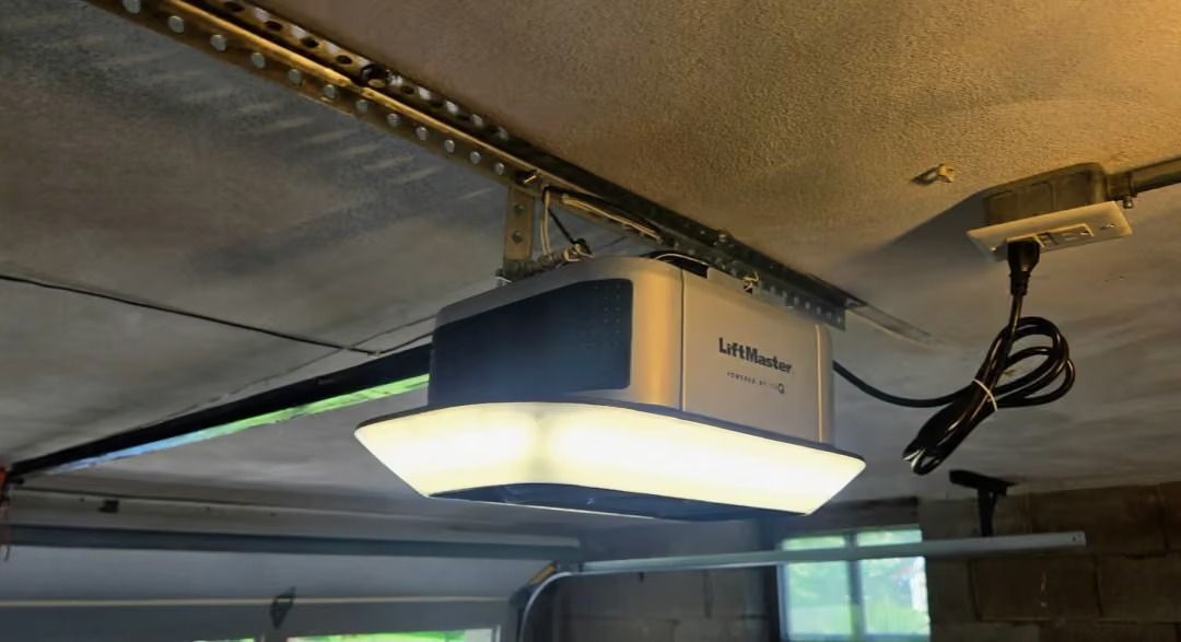 Garage door opener mounted on a ceiling track, with a lit light panel below it.