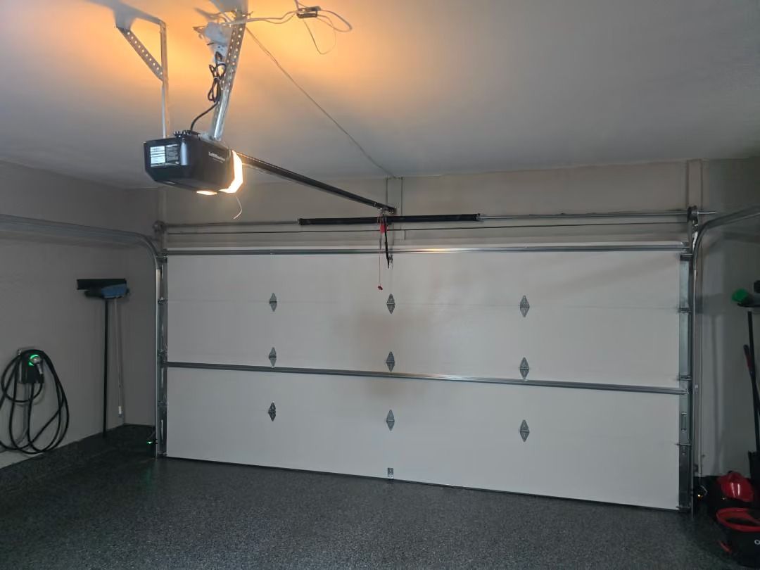Empty garage with a white overhead door, ceiling-mounted opener, and warm overhead lighting.