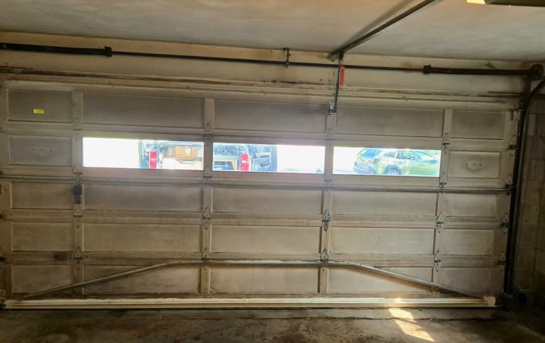 Interior of a garage with a closed metal door and three small windows showing daylight outside.