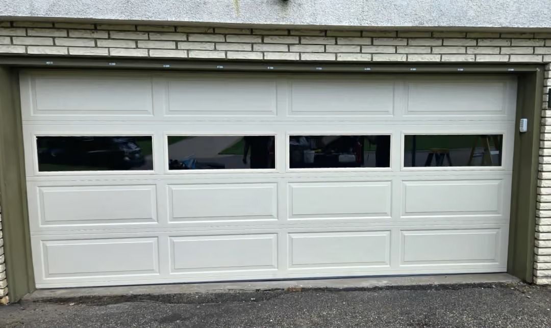 White double garage door with four small windows, set in a beige exterior wall.