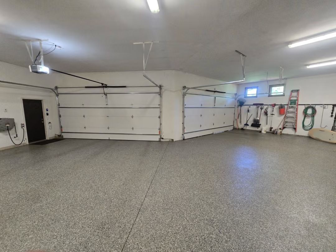 Spacious garage with white walls, closed garage doors, and speckled gray floor under bright ceiling lights