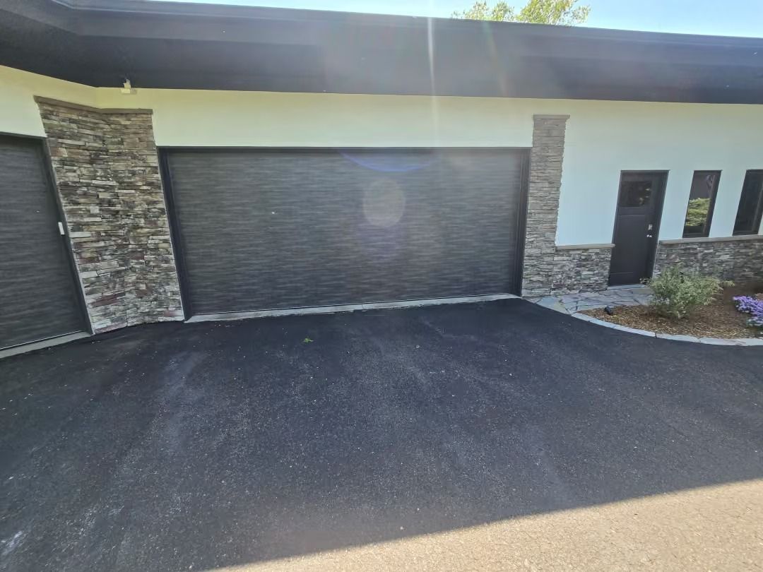 Modern building exterior with dark garage door, white walls, stone accents, and paved driveway