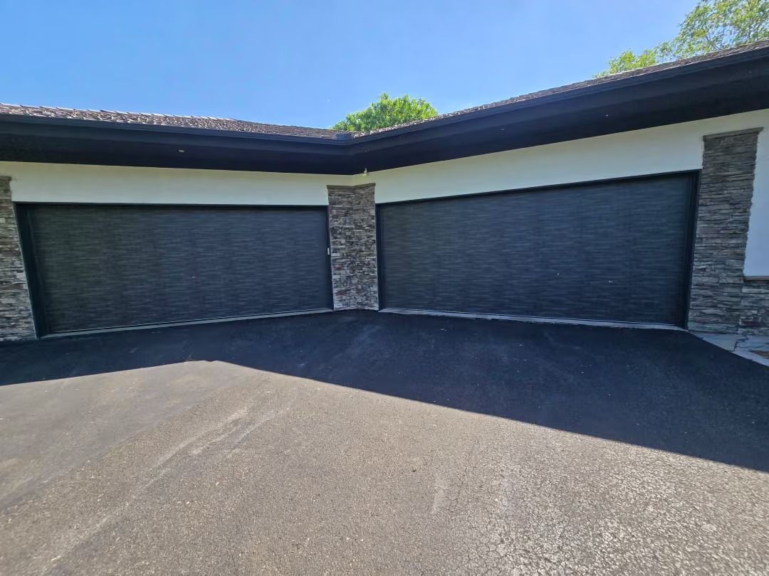 Modern home driveway with three closed gray garage doors and stone accents under a blue sky