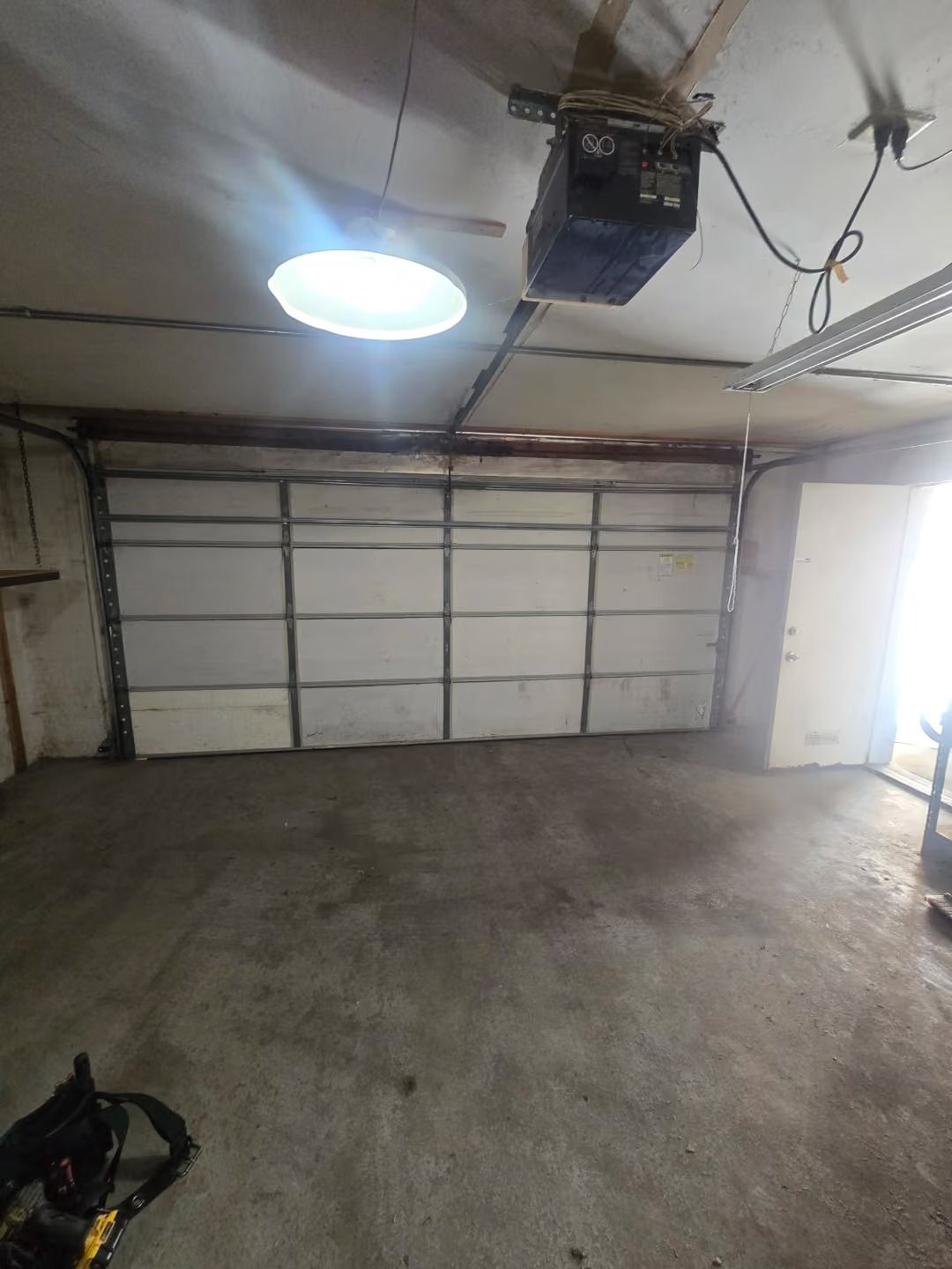 Empty garage with concrete floor, closed white overhead door, and a ceiling-mounted garage door opener.