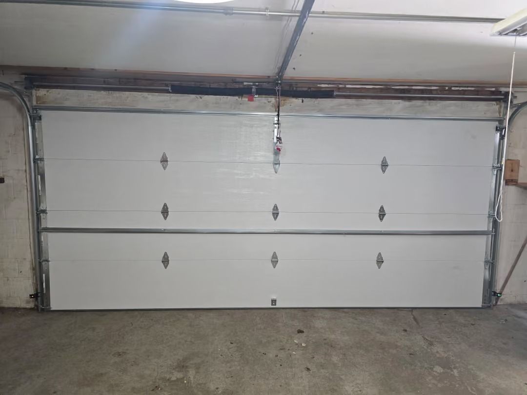 White two-car garage door with metal hinges and opener track in a concrete garage.