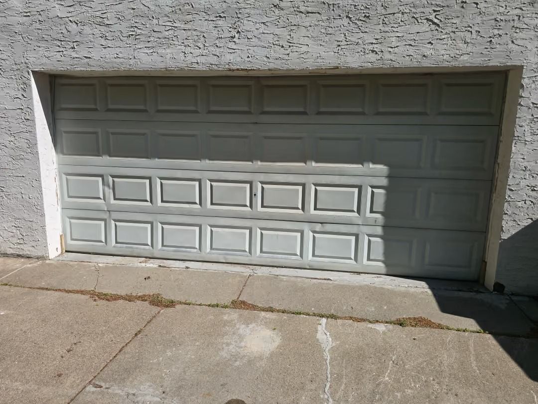 White garage door with a shadow across the lower half and a concrete driveway in front